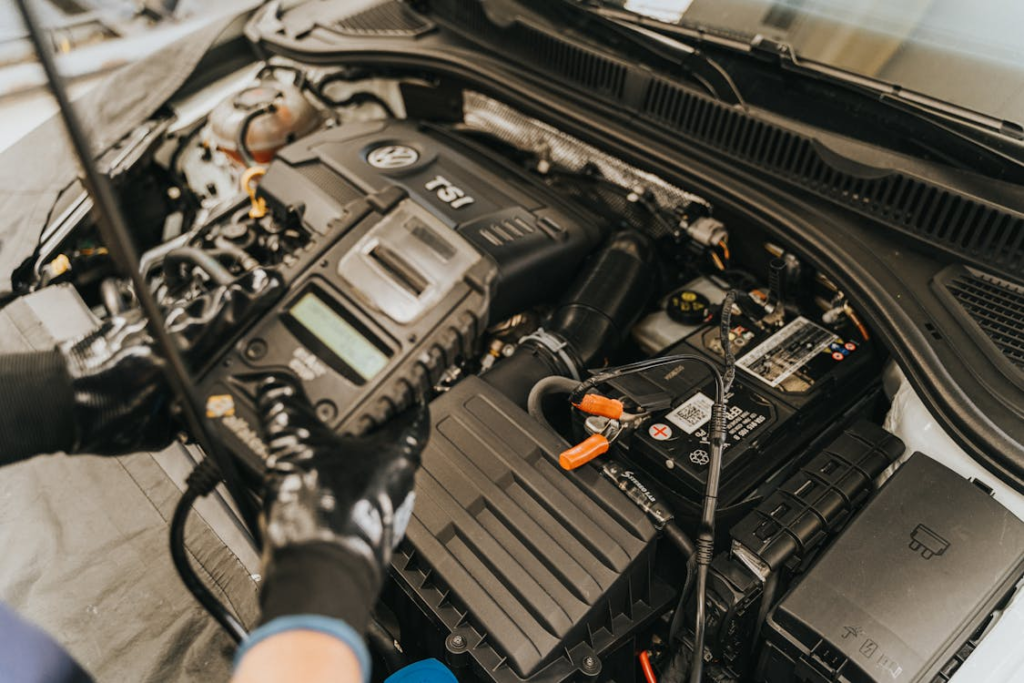 Mechanic using a diagnostic scanner on a Volkswagen TSI engine, wearing black gloves while inspecting the engine components under the hood.